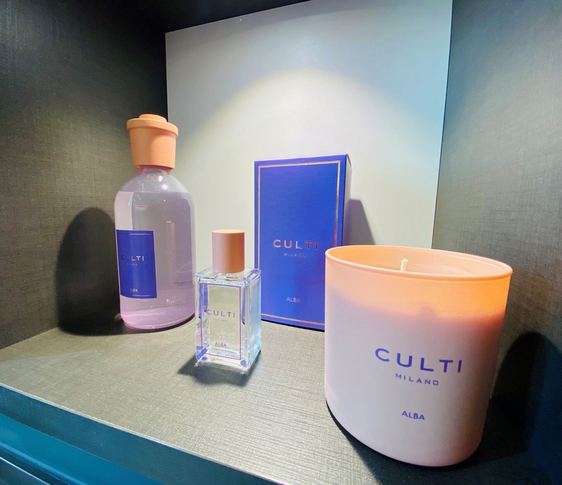 Una collezione di profumatori per ambienti Culti Milano che include un diffusore, un profumo, una confezione regalo e una candela rosa su uno scaffale.