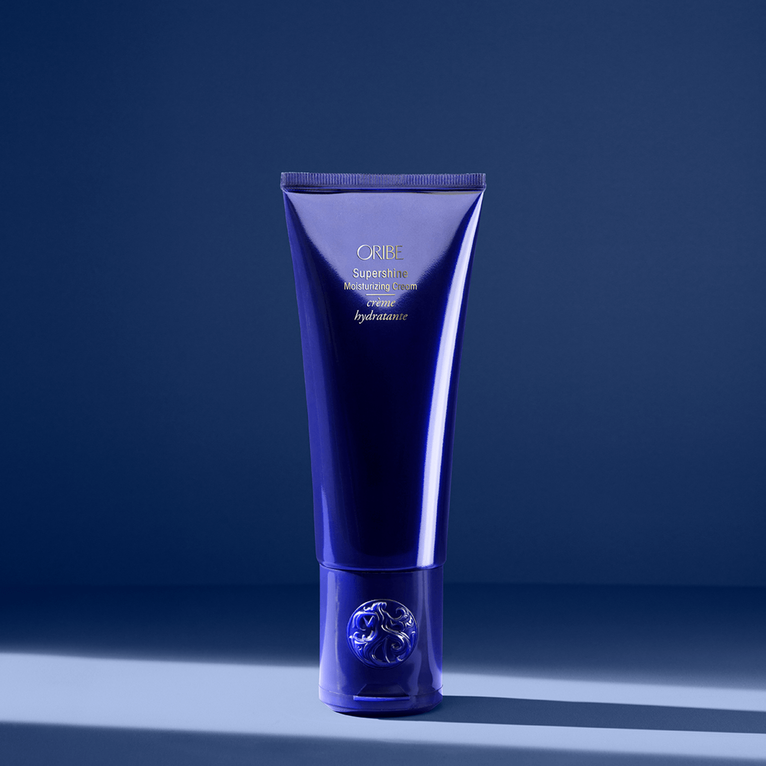 Un tubetto blu intenso di crema Tatcha The Indigo Cream è posizionato verticalmente su uno sfondo blu coordinato, illuminato da una luce soffusa.