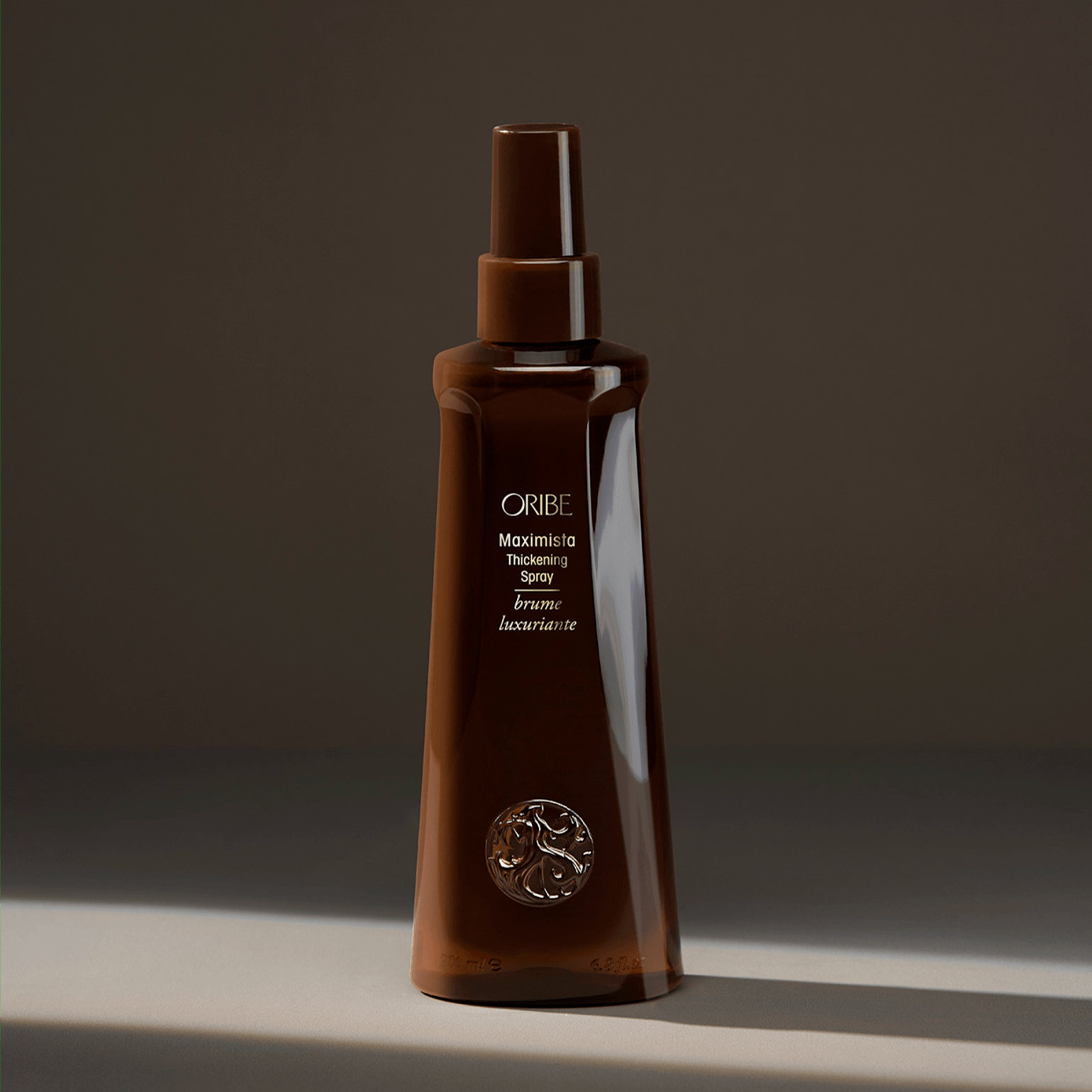 Un flacone spray marrone di Oribe Moisture & Control Deep Treatment Masque, centrato su uno sfondo grigio scuro.