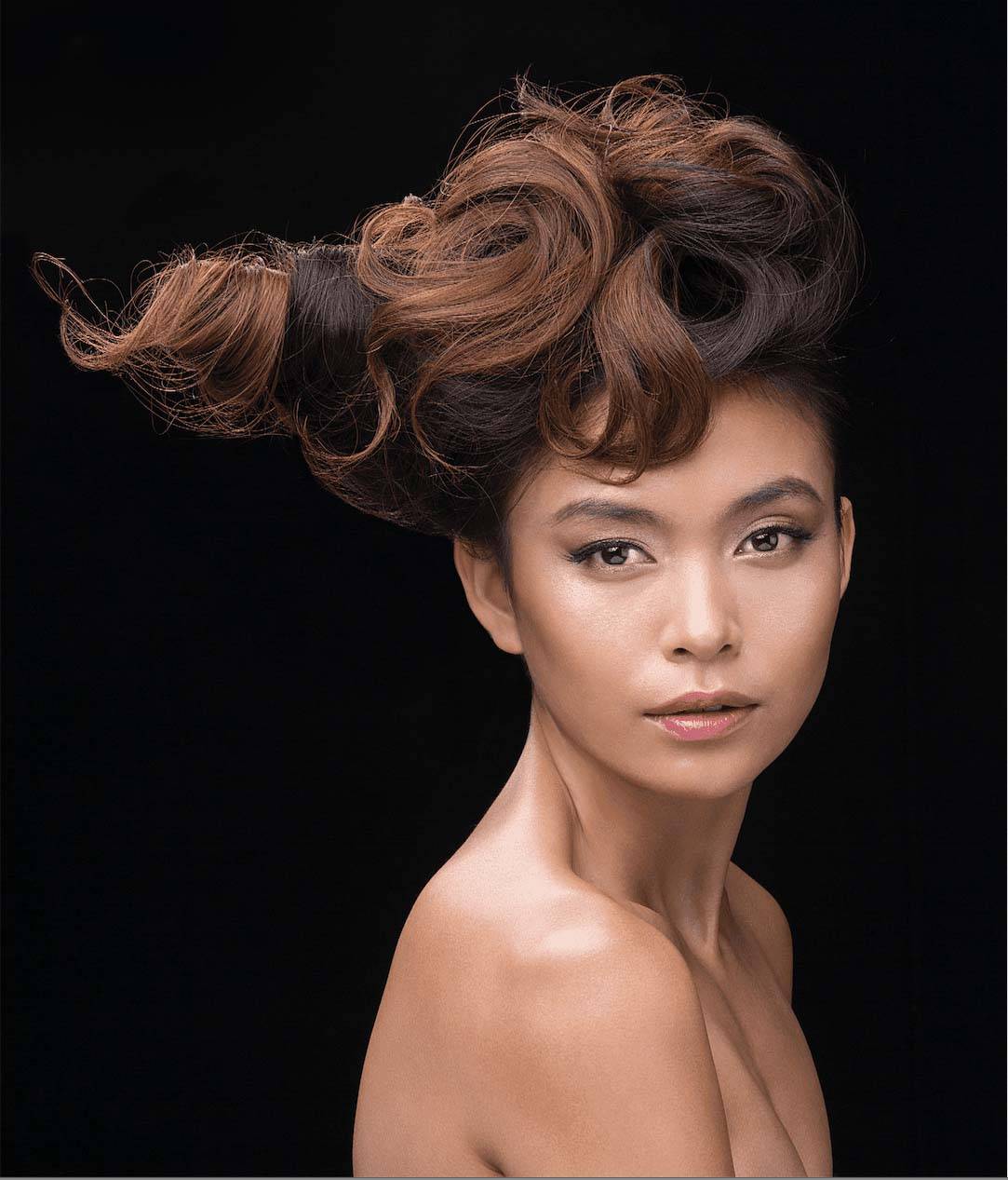 Ritratto di una persona su sfondo nero, caratterizzata da un'elaborata acconciatura con capelli castani scolpiti in curve texturizzate.