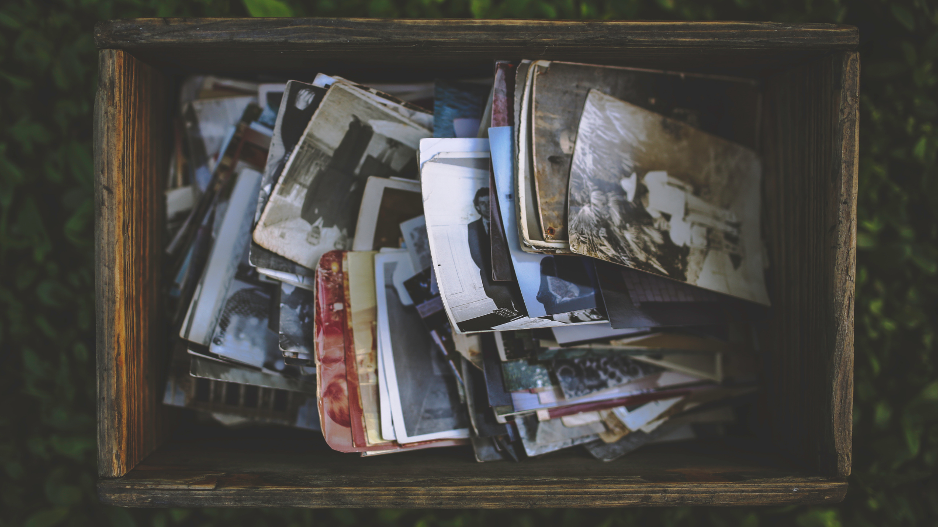 A wooden crate filled with a stack of old photographs and prints.
