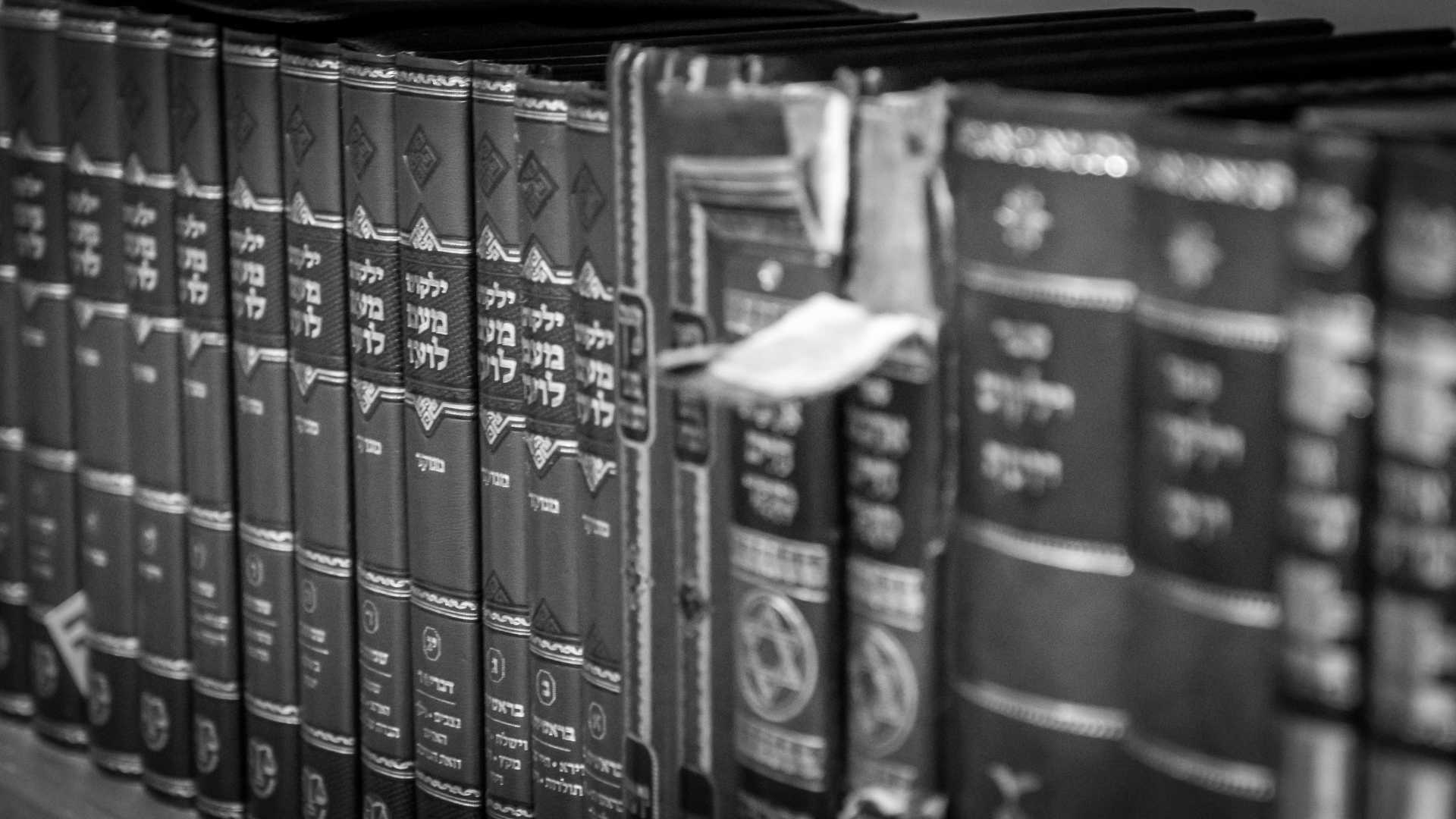 Rows of old leather-bound books on a library shelf, mostly black and white