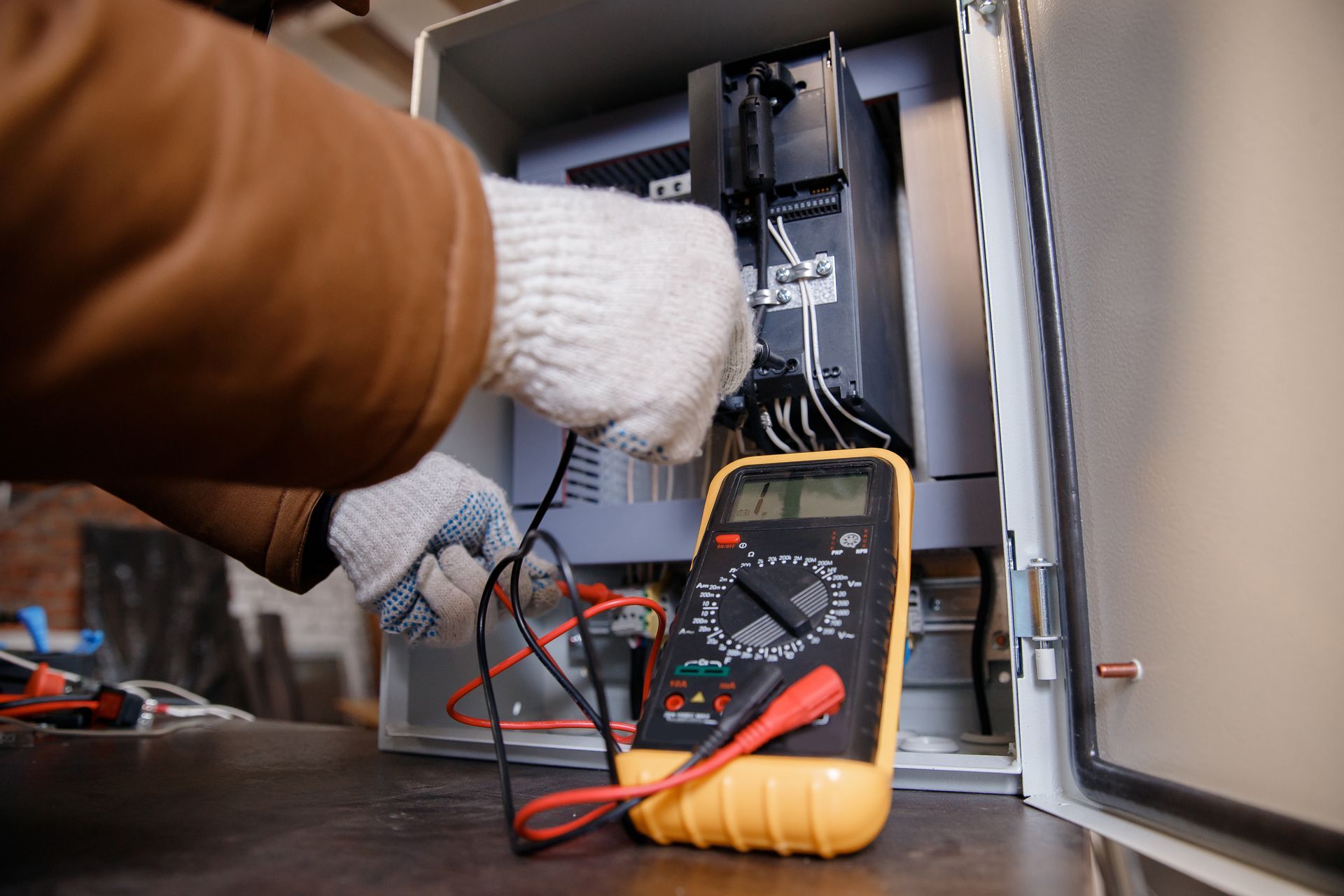 Gloved electrician testing wiring inside an open electrical panel with a multimeter.