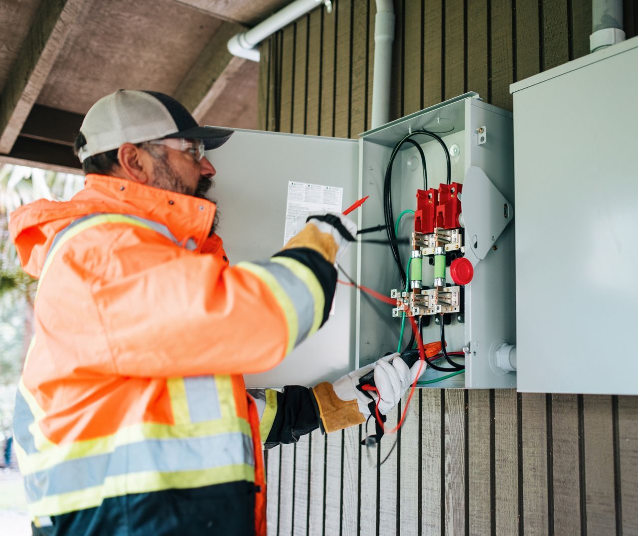 A man in an orange jacket is working on an electrical box.