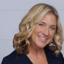 Smiling blonde woman with shoulder-length wavy hair against a light gray background