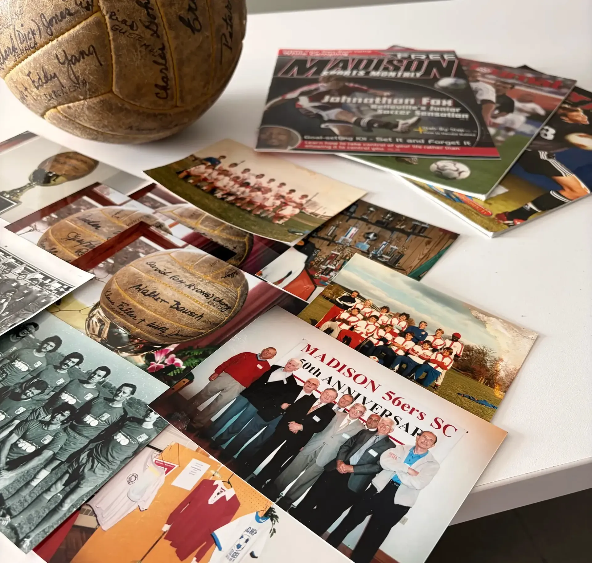 Scattered sports photos, flyers, and a signed basketball on a white table.