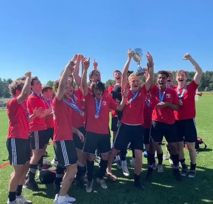 Soccer team in red jerseys celebrating on a sunny field with medals raised overhead