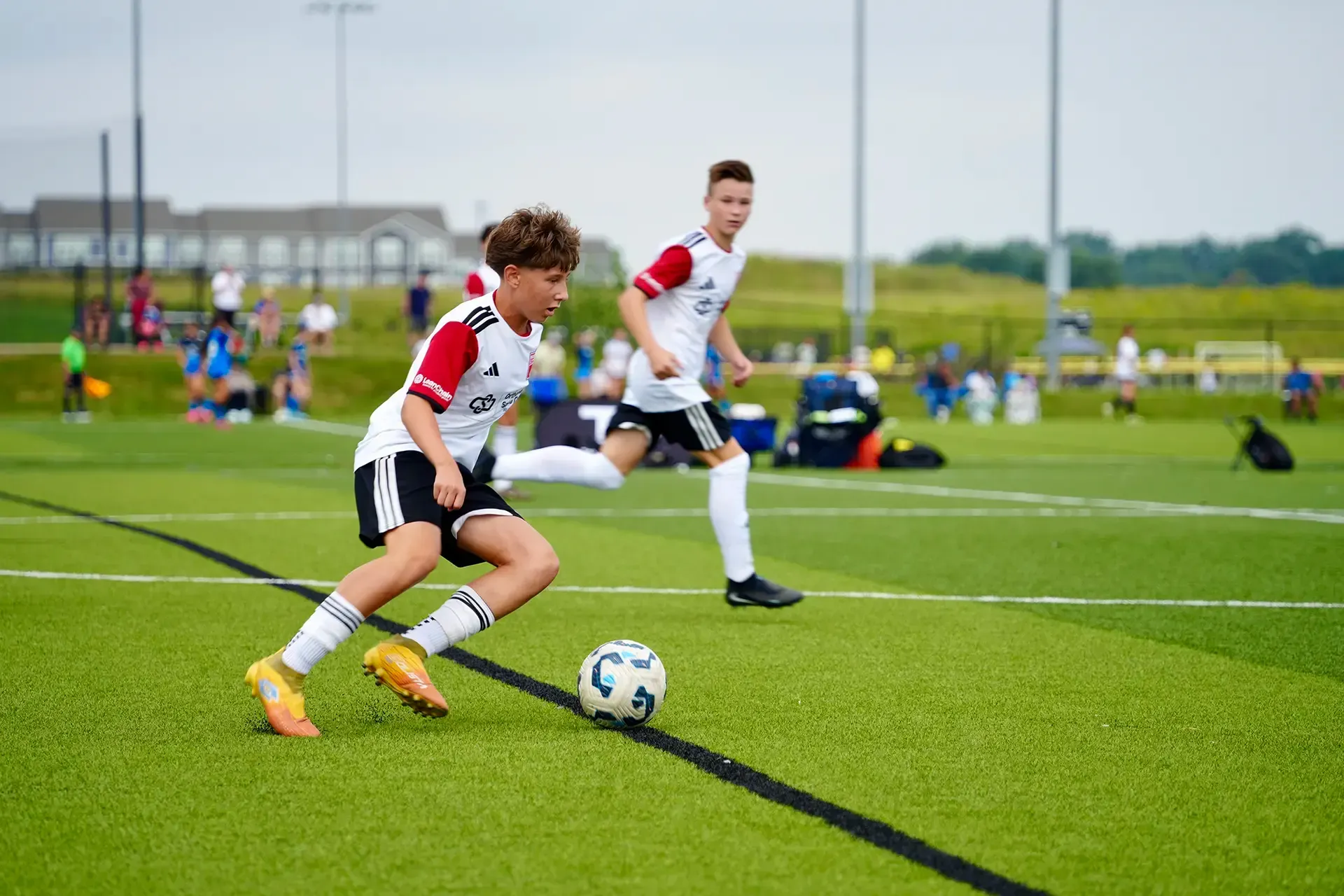 Two soccer players in white and red chase the ball on a green field