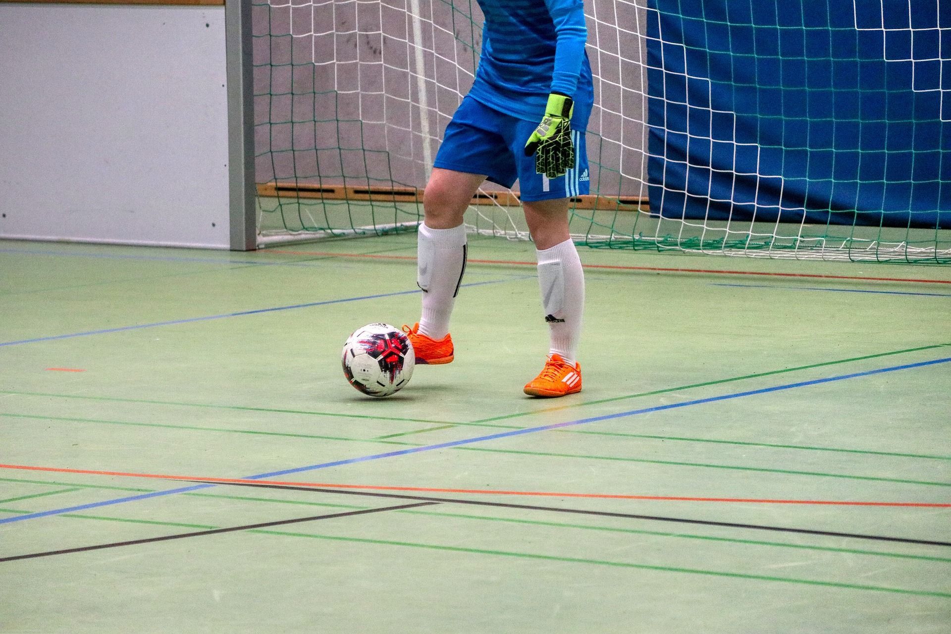 Indoor soccer player in blue and white uniform dribbling a ball near the goal