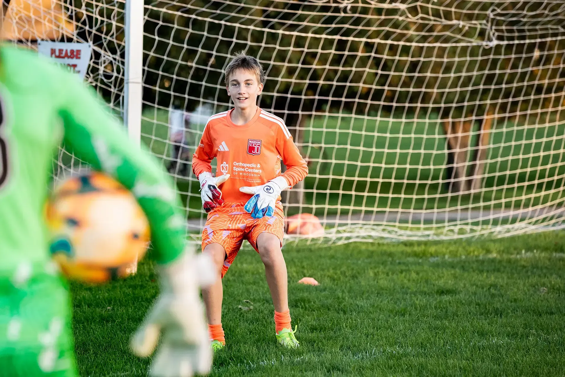 Soccer goalkeeper in orange uniform stands in front of the goal, ready to make a save.