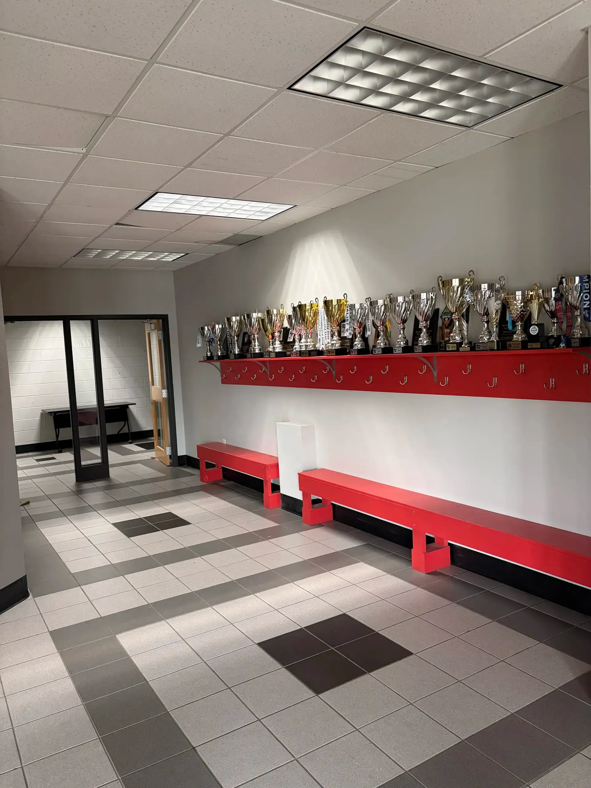 Hallway with red benches, trophy display, tiled floor, and open door at the end