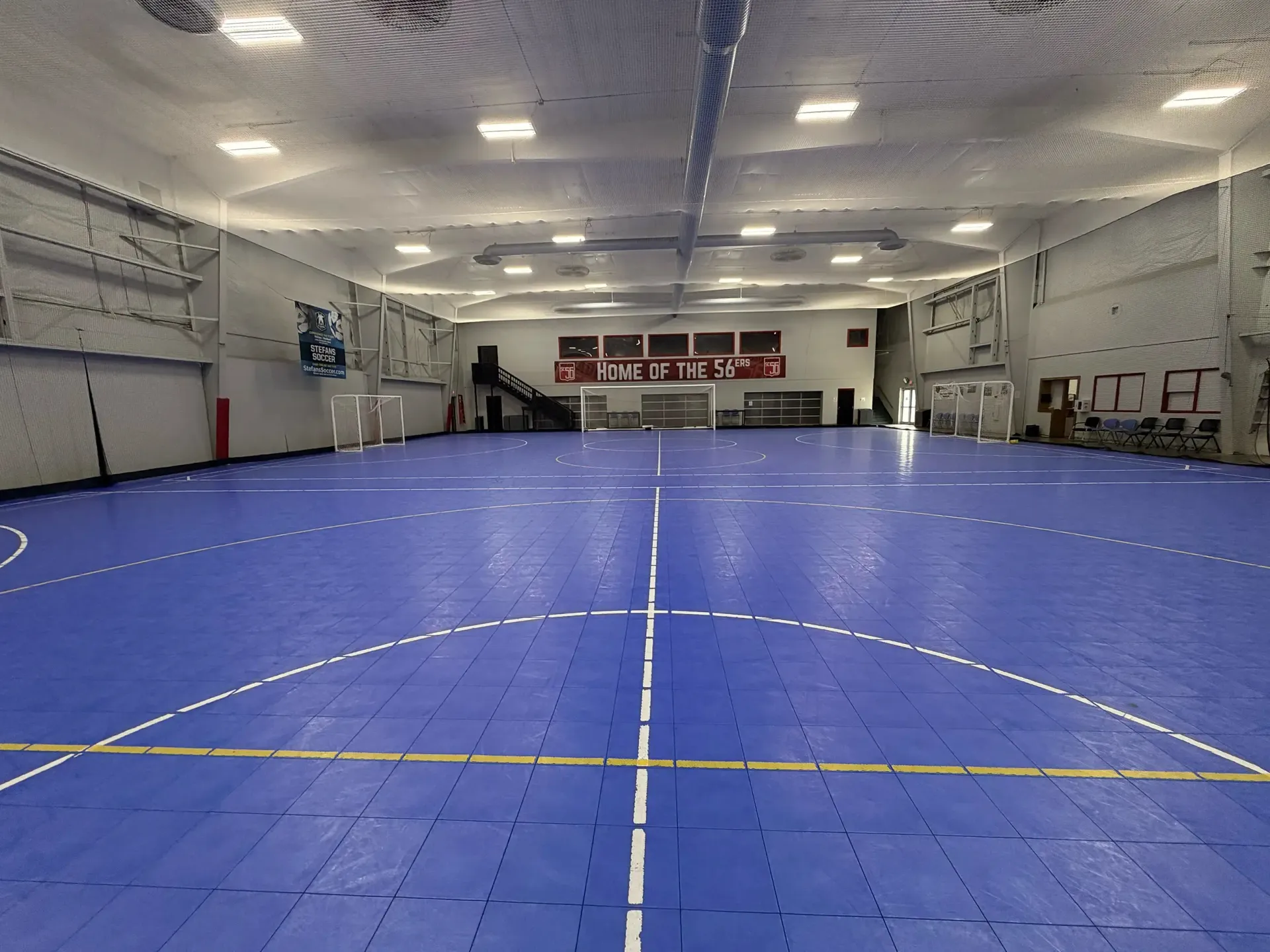 Empty indoor sports court with a blue floor and white ceiling lights