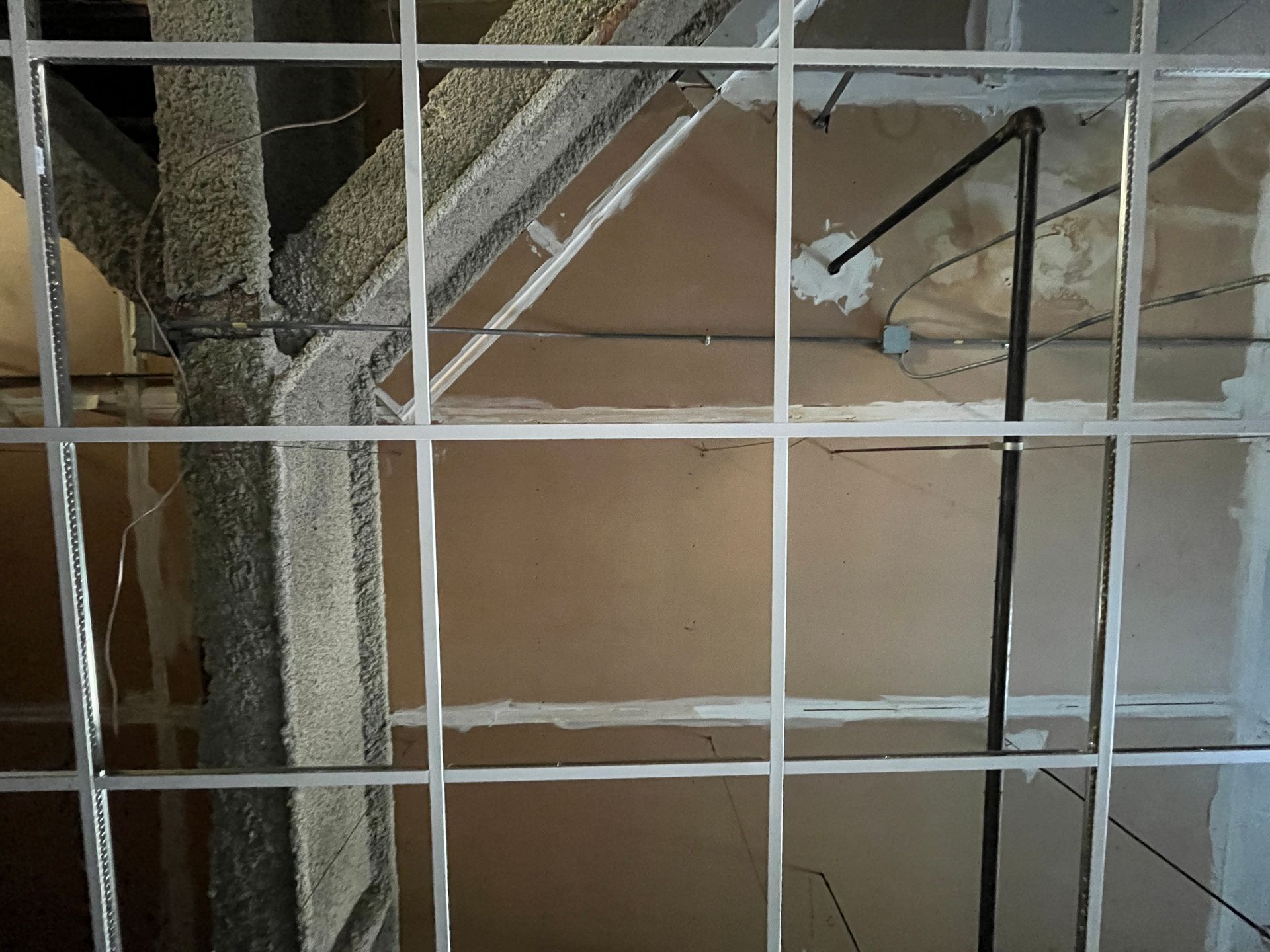 Open ceiling with metal grid and visible textured beams and pipes