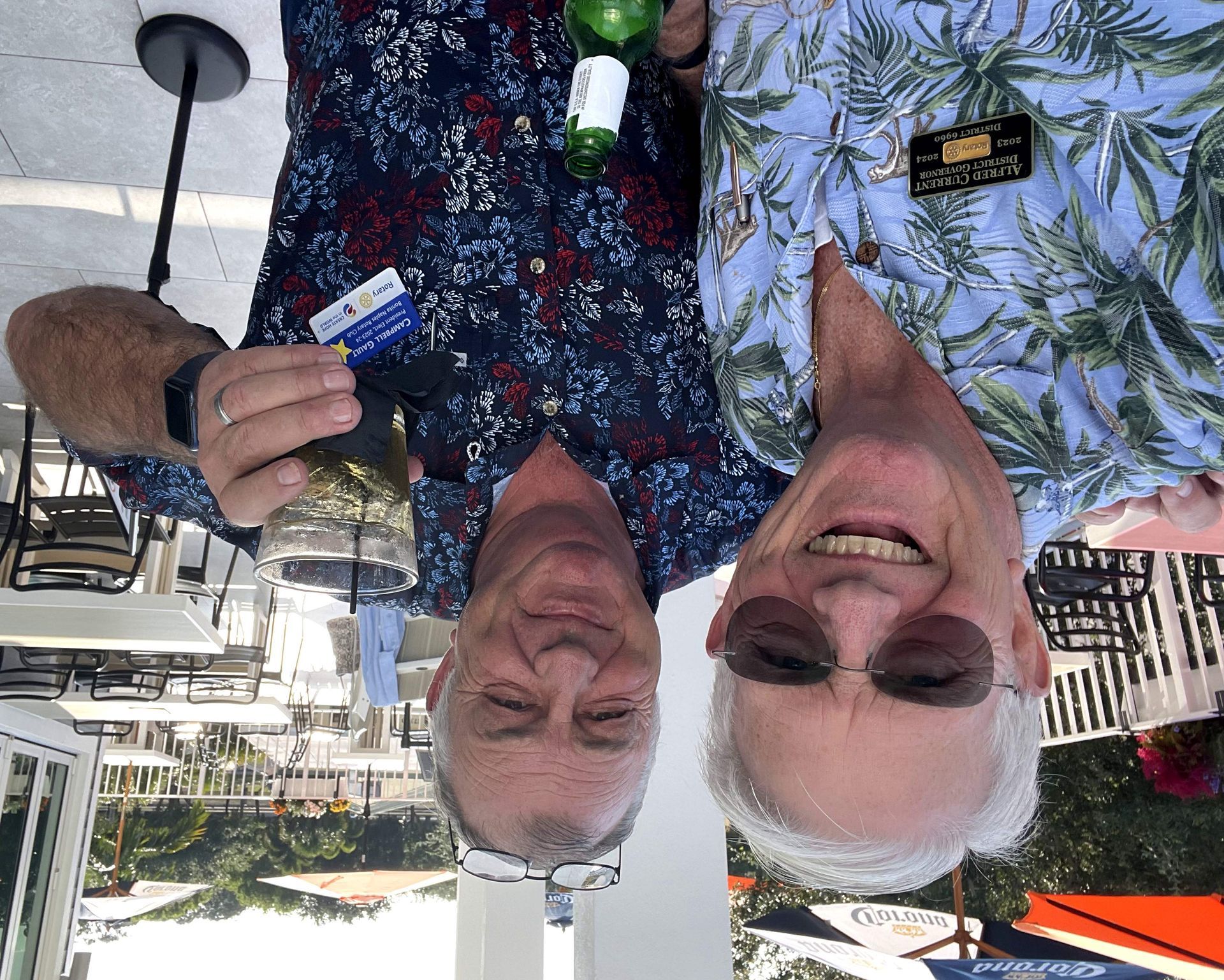 Two men are standing next to each other holding drinks and smiling.