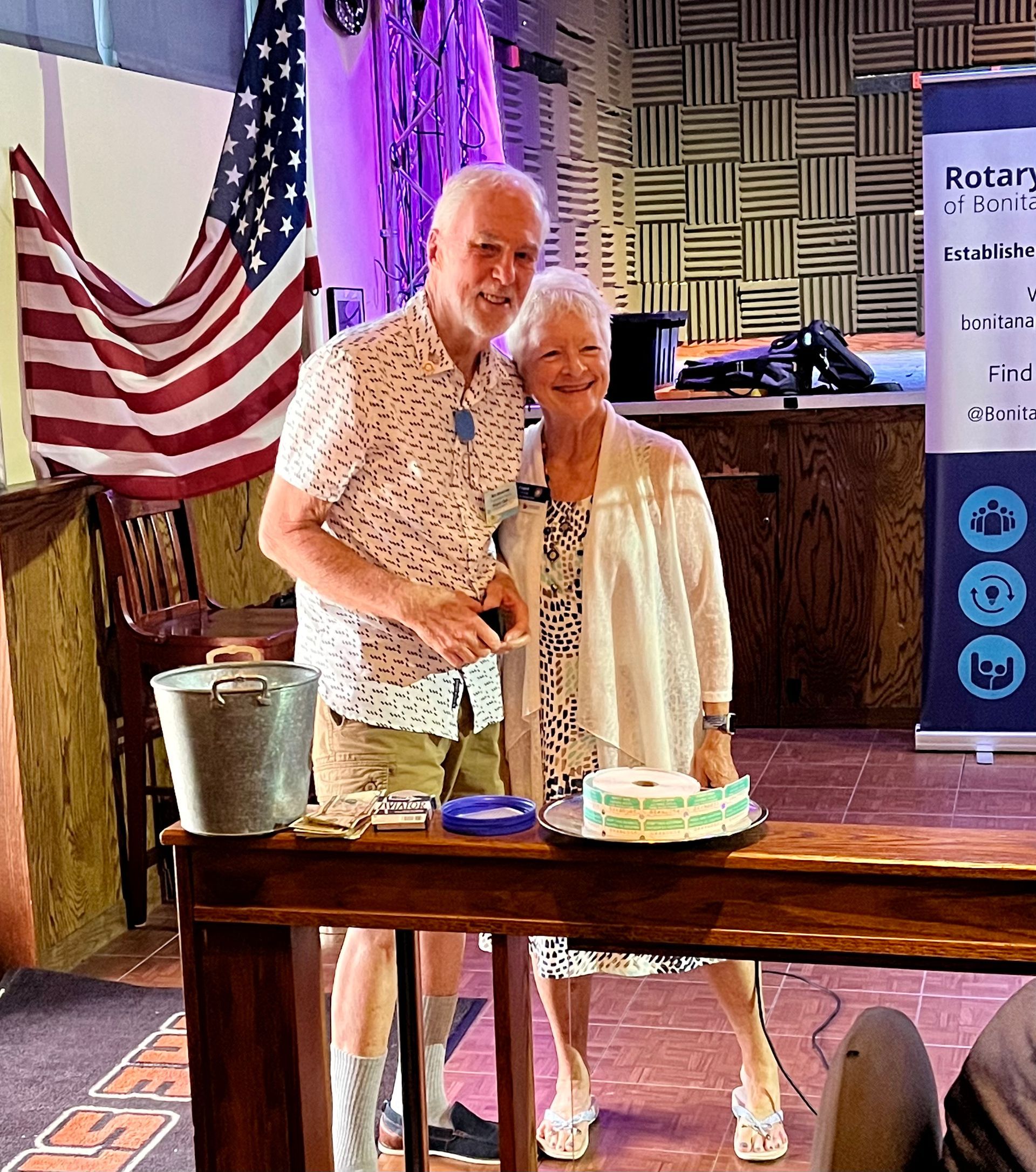 A man and a woman are standing next to a table with a cake on it.