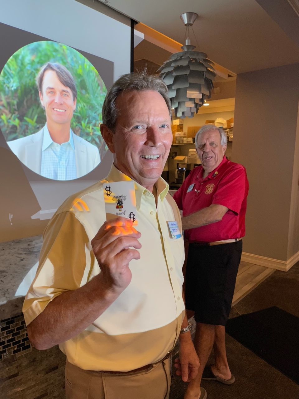 A man in a yellow shirt is holding a card in front of a projector screen.