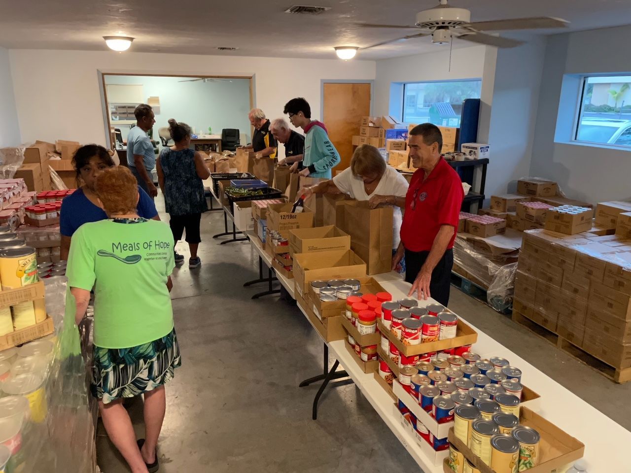 A group of people are standing around a table filled with cans of food.