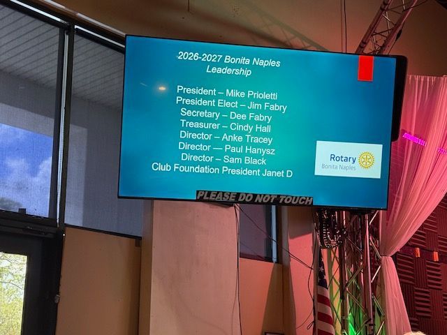 Projected Rotary Club meeting agenda on a blue screen in a banquet hall