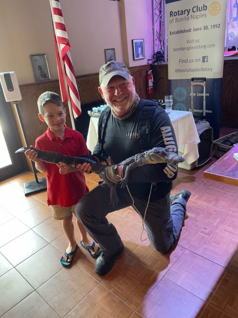A man is kneeling down next to a boy holding a snake.