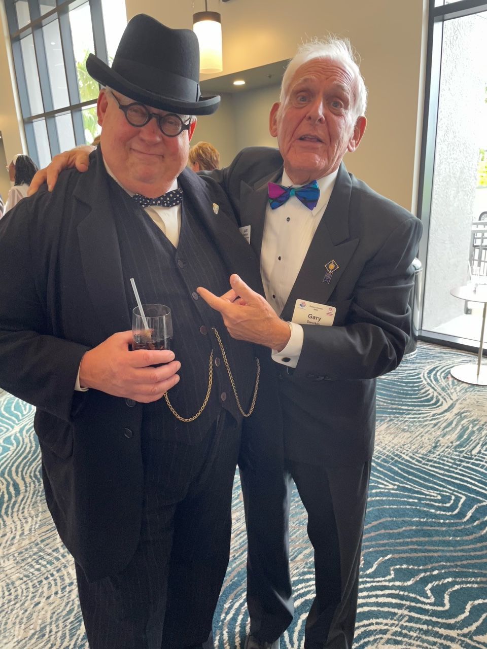 Two men in suits and hats are posing for a picture