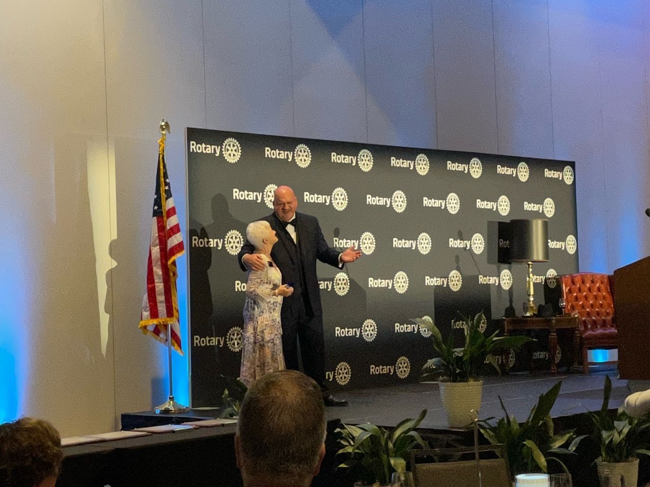 A man and woman are standing in front of a wall that says rotary