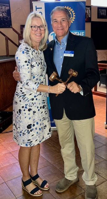 Two people smiling and shaking hands at an indoor event, holding a small wooden award.