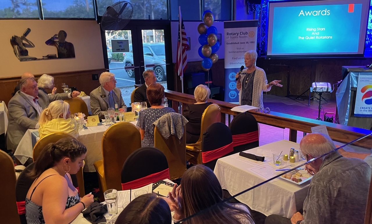 A woman is giving a presentation to a group of people sitting at tables in a restaurant.