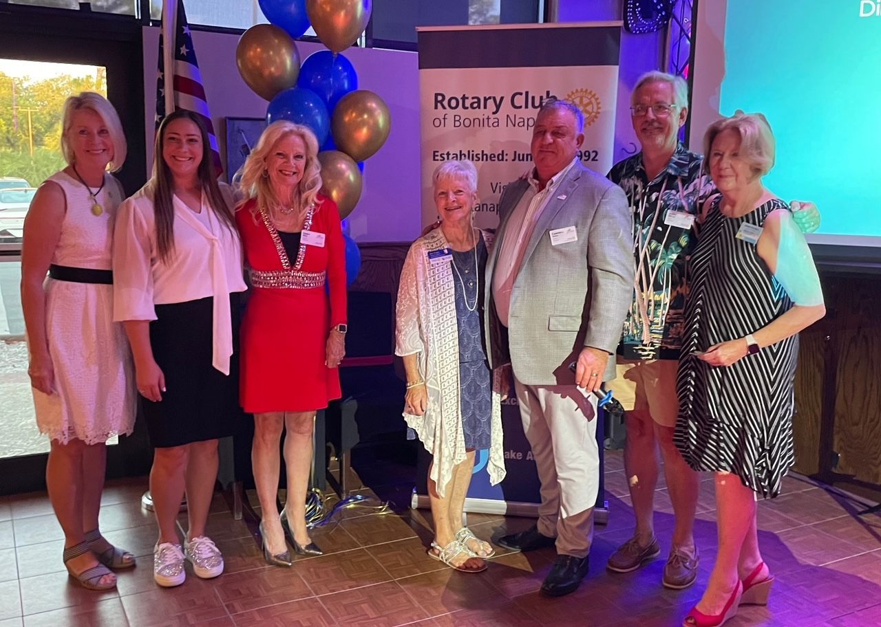 A group of people are posing for a picture in front of a sign that says rotary club.