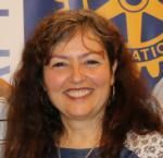 A woman with long hair is smiling in front of a rotary logo.