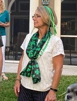 A woman wearing a green scarf and a green headband is standing in the grass next to a dog.