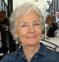 A woman is sitting at a table in a restaurant wearing a denim shirt and earrings.