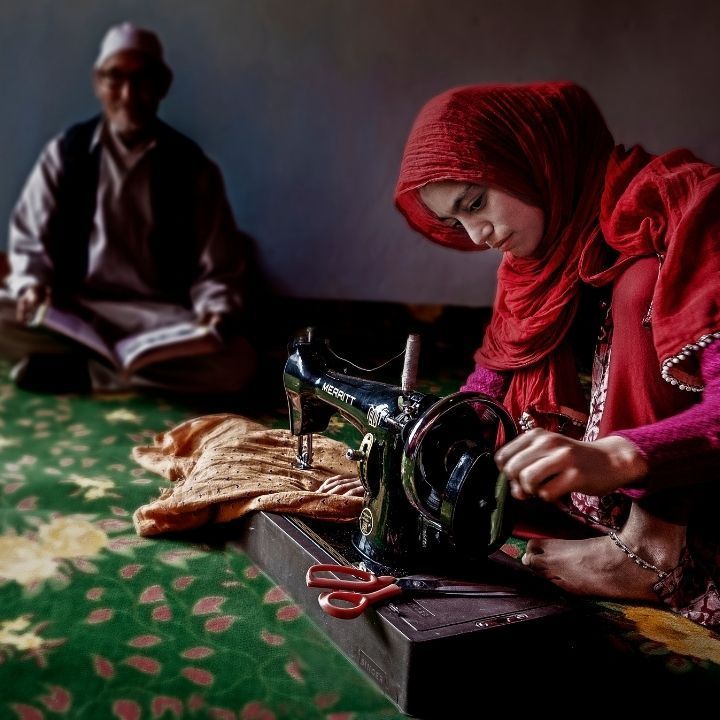 A woman in a red hijab is using a sewing machine
