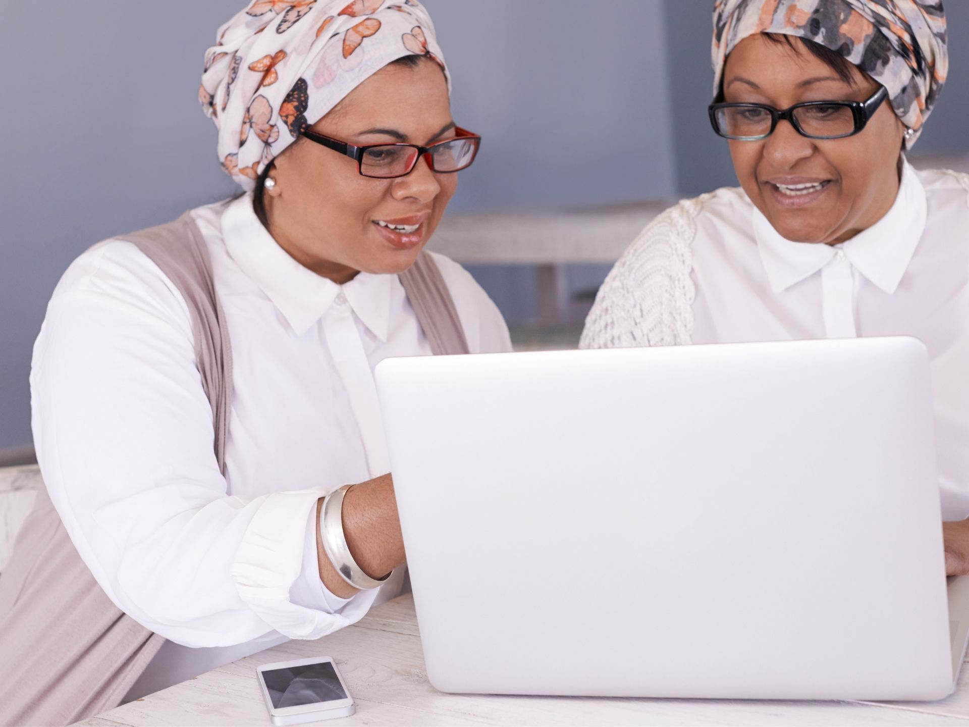 Two women are looking at a laptop together and smiling