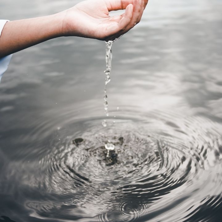 A person is pouring water from their hand into a body of water.