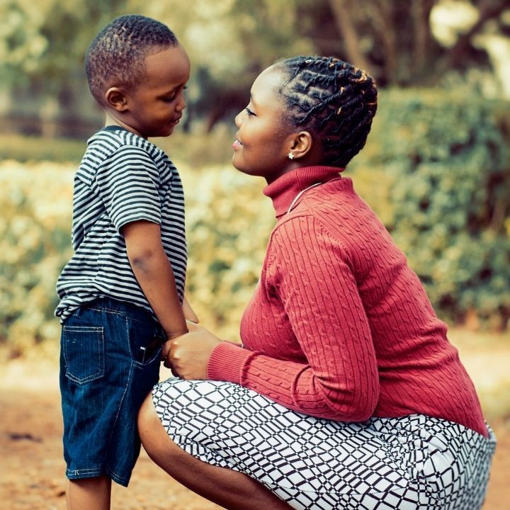 A woman is kneeling down next to a little boy and holding his hand.