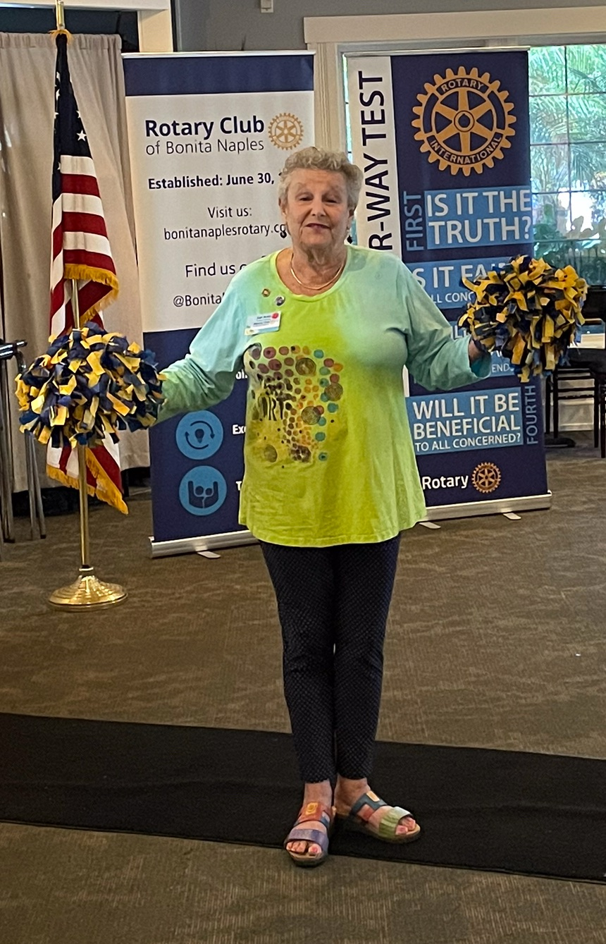 A woman in a green shirt is standing in front of a rotary club banner.