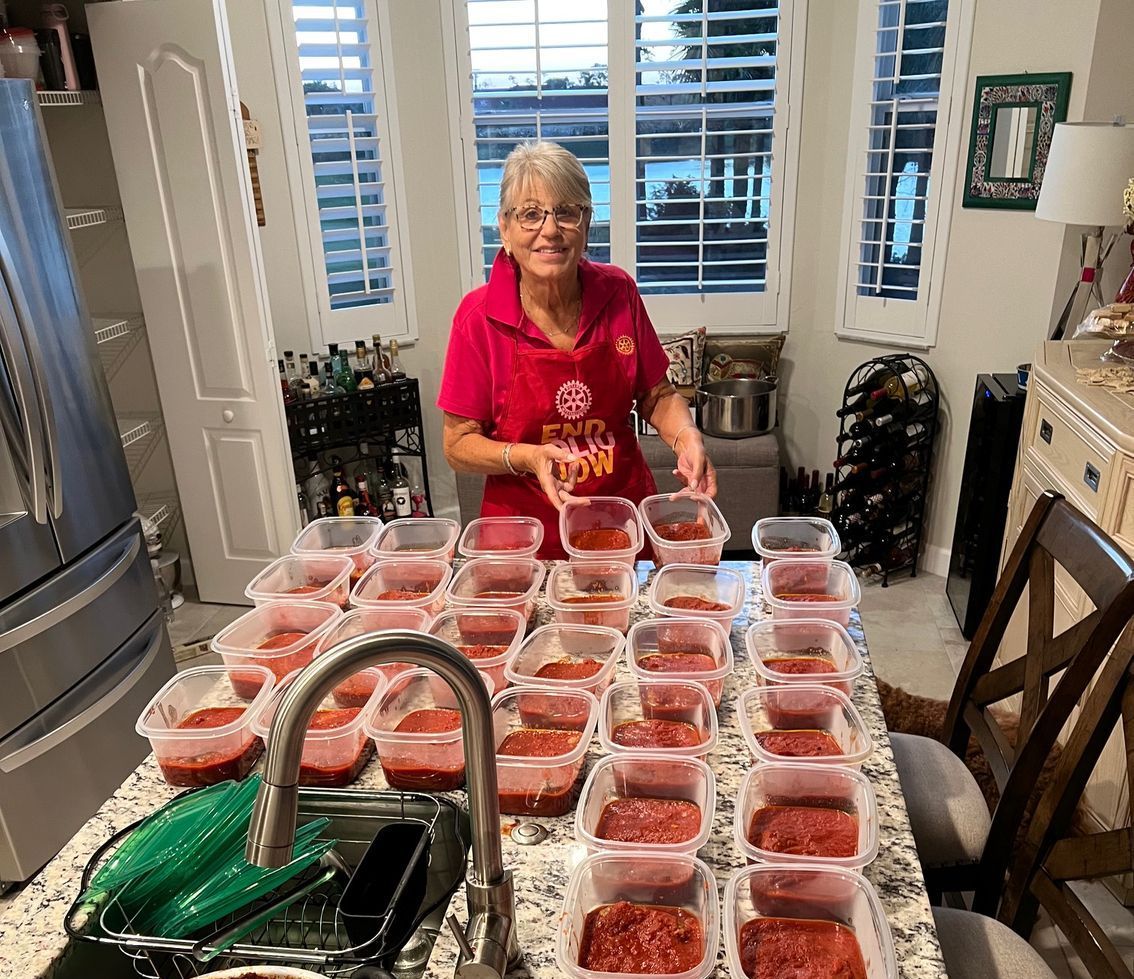 A woman is standing at a kitchen counter filled with plastic containers of food.