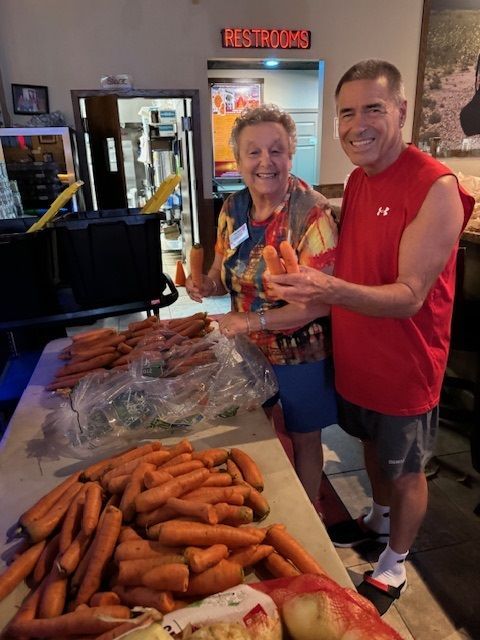 A man and a woman are standing in front of a table full of carrots.