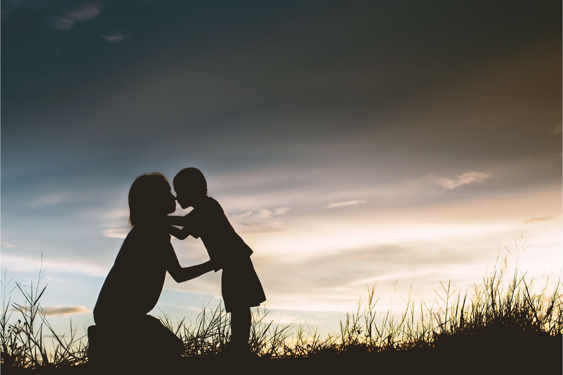 A silhouette of a mother and daughter kissing at sunset.