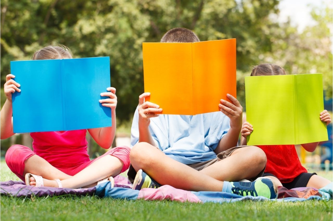 A group of children are sitting on the grass reading books.