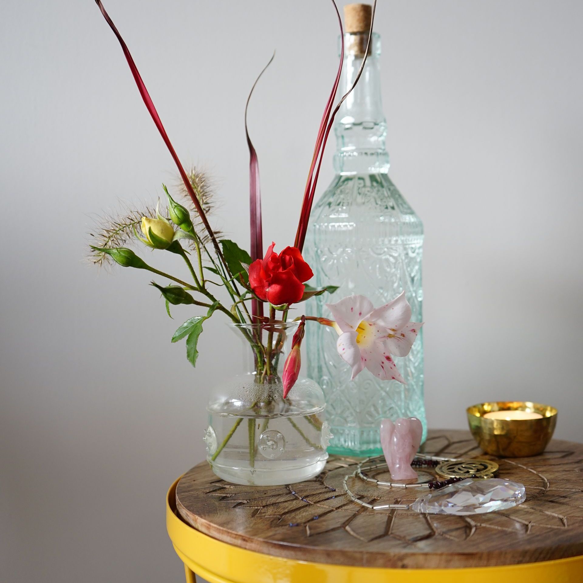 Op een gele tafel staan ​​vazen ​​met bloemen, een fles en sieraden.