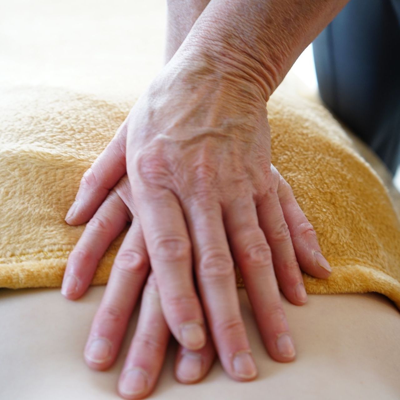 Handen masseren de rug van een persoon, bedekt met een gele handdoek.