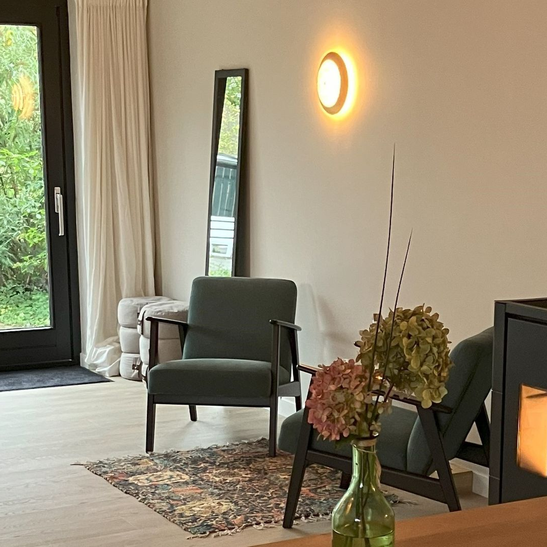 Gezellige praktijkruimte met groene fauteuils, een spiegel en bloemen.
