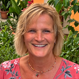 Vrouw (eigenaar Senti) met kin op haar hand, glimlachend. Leunend op de grond, binnenshuis. Zwart shirt.