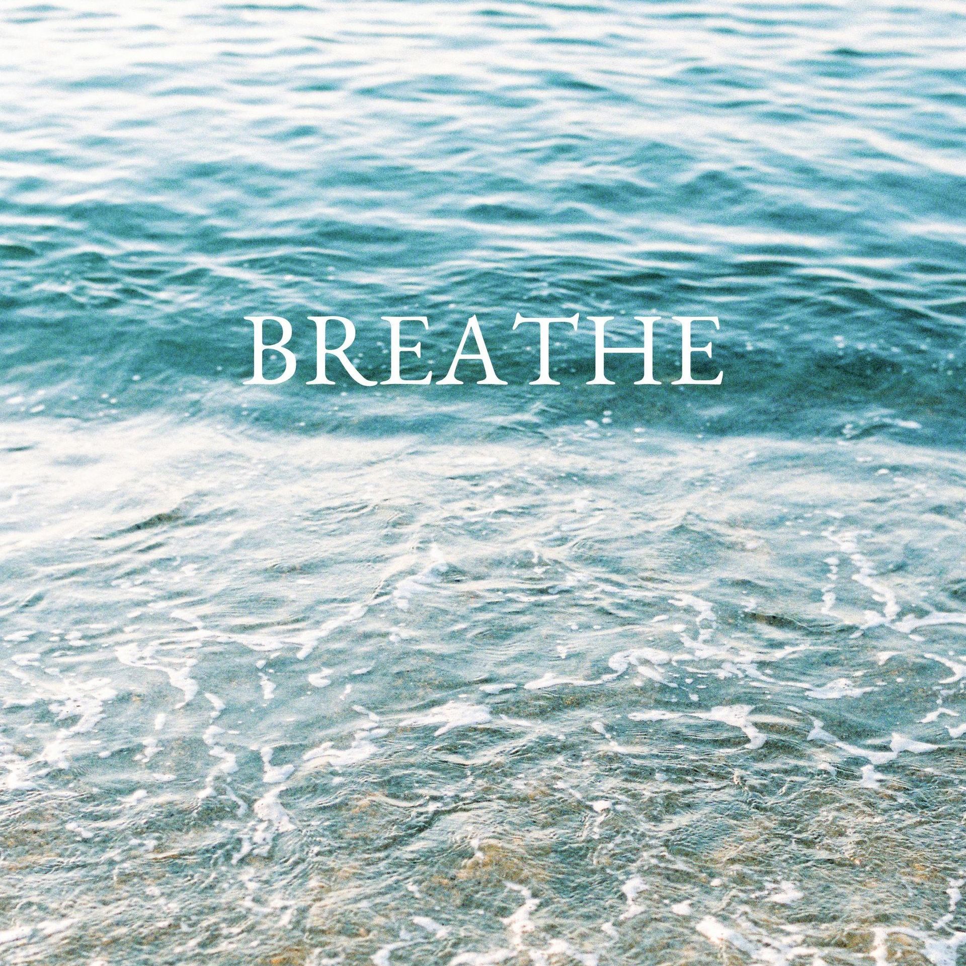 Golven die zachtjes aanspoelen op het strand met de tekst 'Breathe' eroverheen.