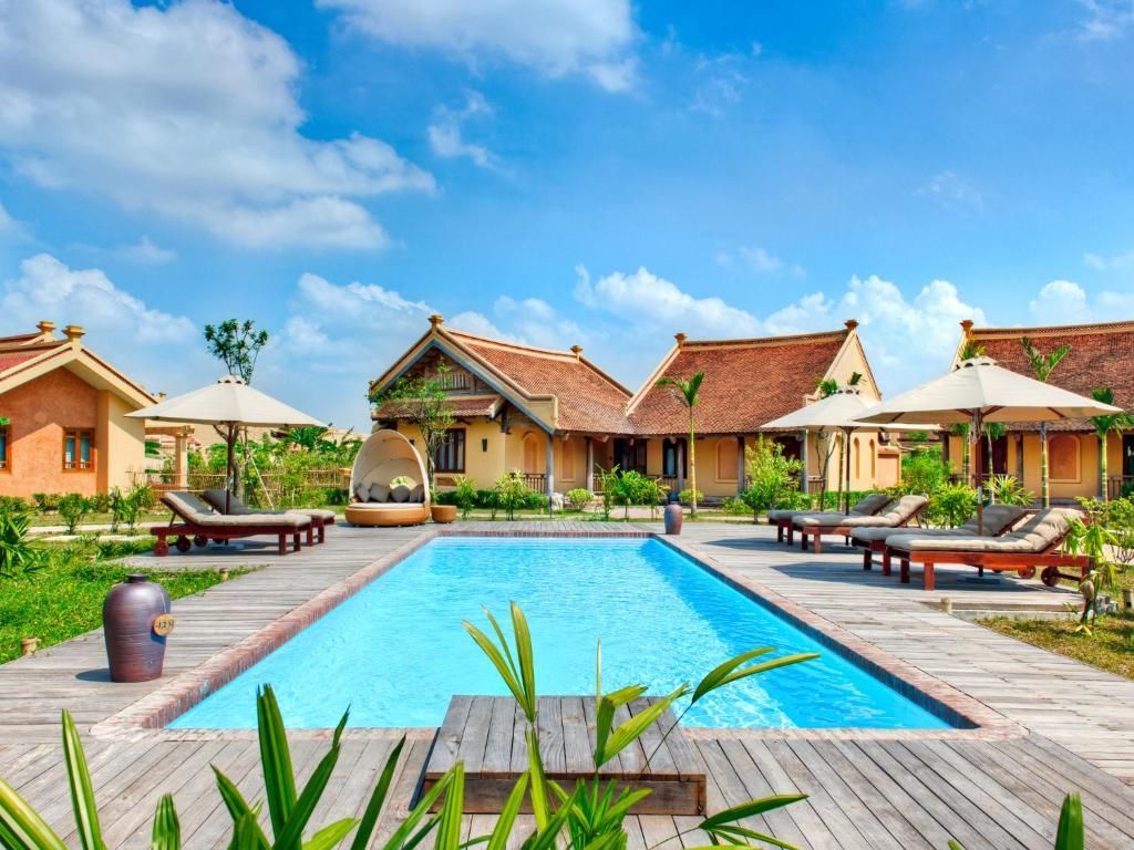 Swimming pool and lounge chairs at a resort with bungalows under a blue sky.