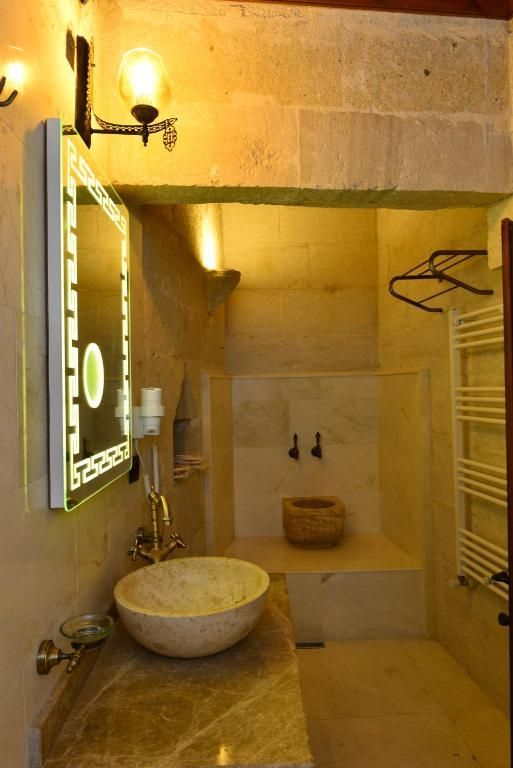 Bathroom with stone walls, marble countertop, round sink, lit mirror, and towel warmer.