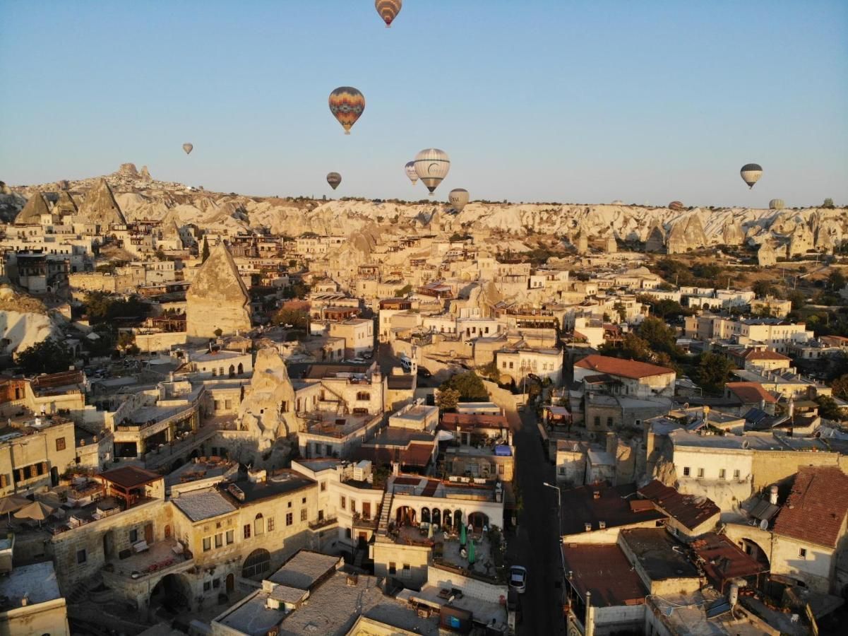 Hot air balloons float over a town of beige buildings and rock formations in Cappadocia, Turkey.