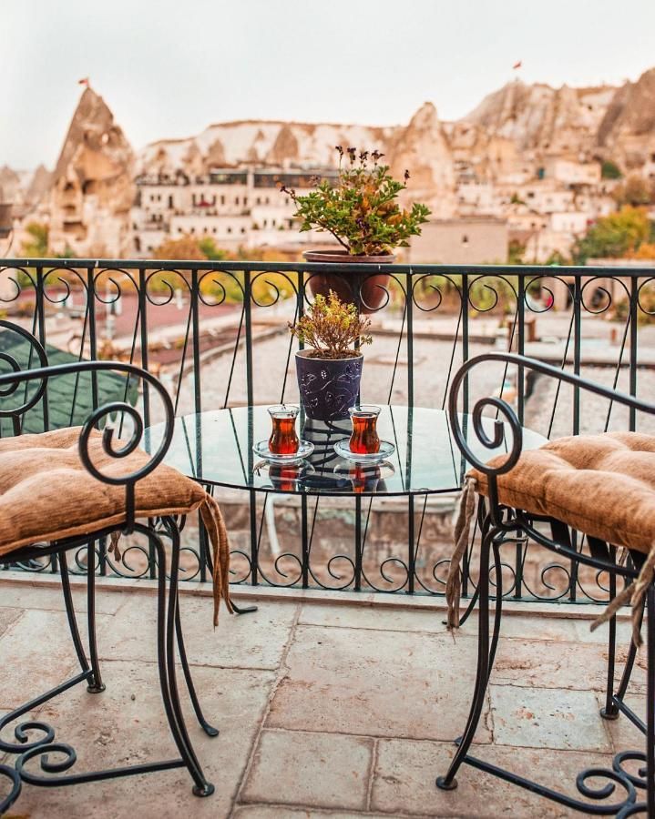 Balcony with table, chairs, teacups, and potted plants overlooking a town in Cappadocia, Turkey.