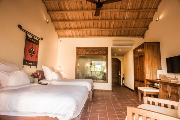 Hotel room with two beds, wooden ceiling, terracotta tile floor, and a large window.